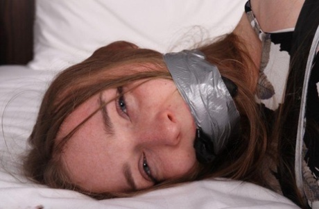 Caucasian female is silenced with gags while restrained upon a bed 24196734