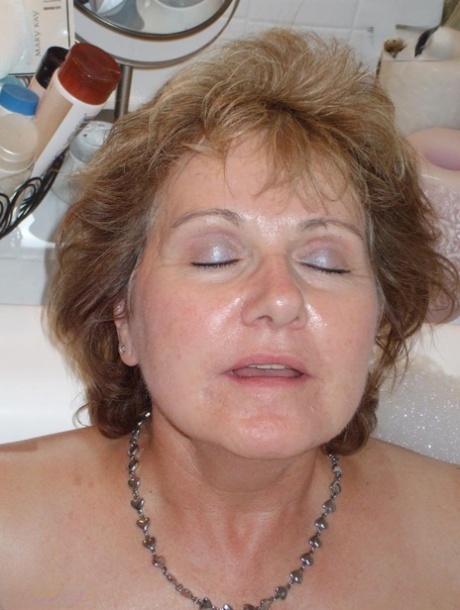 Older amateur Busty Bliss licks her lips during a playful bubble bath